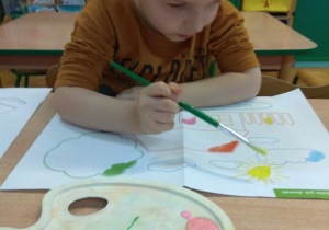 Chłopiec maluje farbami na dużej powierzchni.